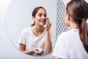 Young woman putting on moisturizer